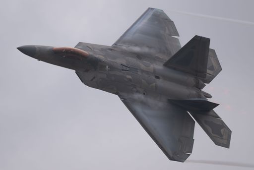 A fighter jet is seen soaring in the clear blue sky, its wings cutting through the air with the sun glistening off its surfaces