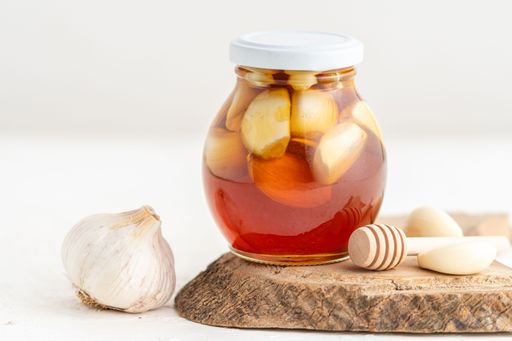 A jar of honey with garlic inside and a honeycomb, on a white background, home remedy for flu with copy space