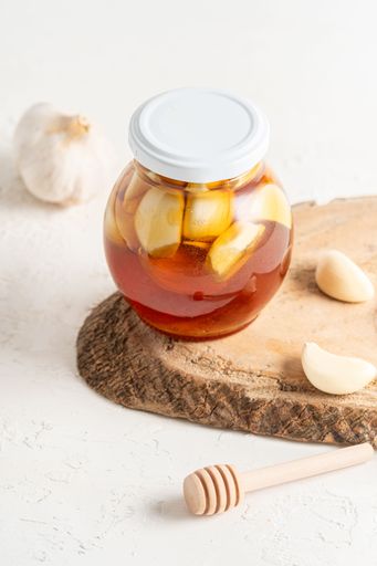 A jar of honey with garlic inside and a honeycomb, on a white background, home remedy for flu with copy space
