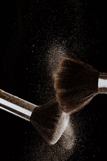 A vertical shot of makeup brushes white powder explosion isolated on a black background