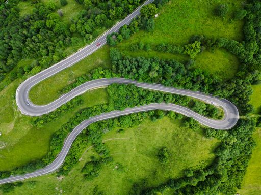 An Aerial view of a winding mountain road in Romania, surrounded by lush green hills