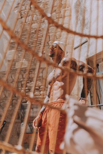 A shirtless male in orange shorts behind a straw chair