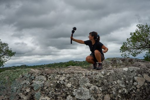 A traveler and blogger crouching and holding an action camera for streaming in natural environment