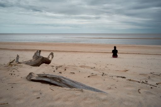 A woman contemplating on sandy beach while looking at the sea - spiritual concept of self-knowledge
