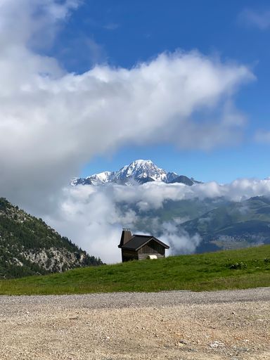A scenic view of a rustic cabin situated in a hilly area against a backdrop of snow-capped mountains