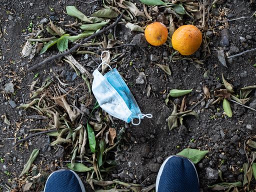 A selective focus shot of oranges a thrown sanitary mask, and sneakers on the ground