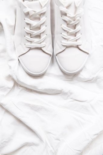 A vertical top view of pristine white sneakers on a white cloth