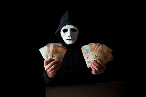 hacker man dressed in black with white mask and black hood holding euro banknotes in his hands, cybercrime concept, isolated on black background