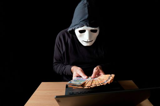 hacker man dressed in black with white mask and black hood counting euro banknotes in his hands, cybercrime concept, isolated on black background