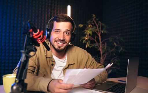 A happy radio presenter wearing headphones and reading news from a paper into a studio microphone in a radio station