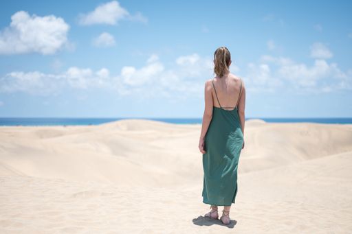 Blond young girl with green dress from behind on the beach dunes