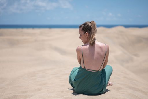 Blonde young girl in green dress sitting on sand of beach dunes