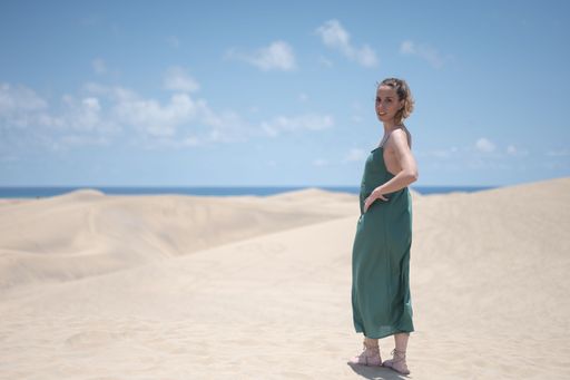 Young blonde girl in green dress with her back turned and looking at the camera in the dunes of the beach