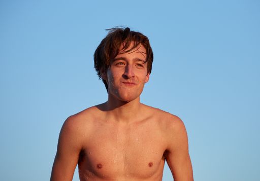 A closeup shot of a caucasian male laughing at a beach with the skies in the background