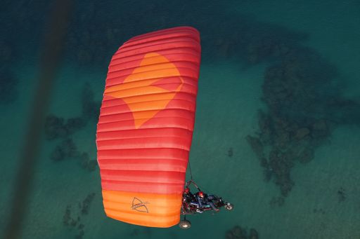 A high angle shot of the powered paraglider flying over the ocean