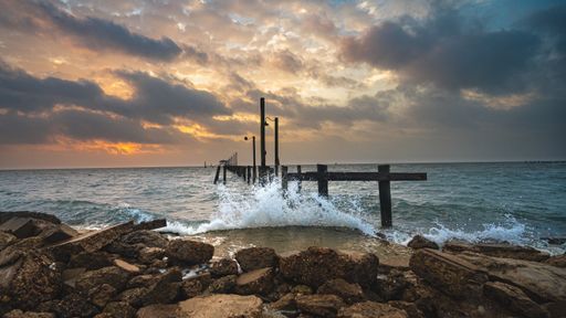 A scenic view of the wavy ocean hitting the rocky beach gleaming under the sunset in the cloudy sky