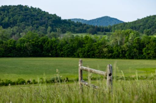 A rustic wooden fence in front of a lush grassy meadow with rolling hills in the background