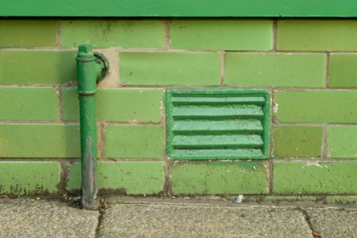 A closeup shot of a green wall with a pipe and a sealed off window