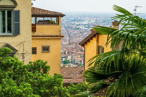 The San Vigilio Castle on the upper city of Bergamo, looking down on the lower city of Bergamo from the castle walls, with green trees.
