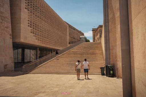 Two people ascend a stairway leading to a majestic archway and grand building