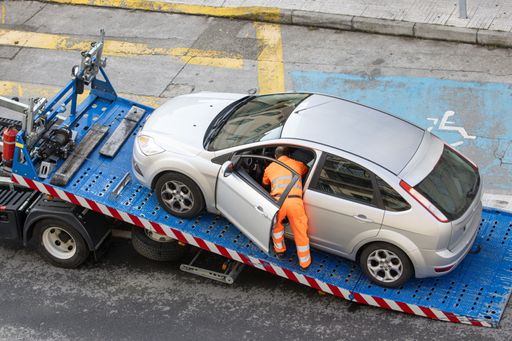 Damaged car being loaded onto tow truck by a worker. Towing service on the city. Roadside assistance concept