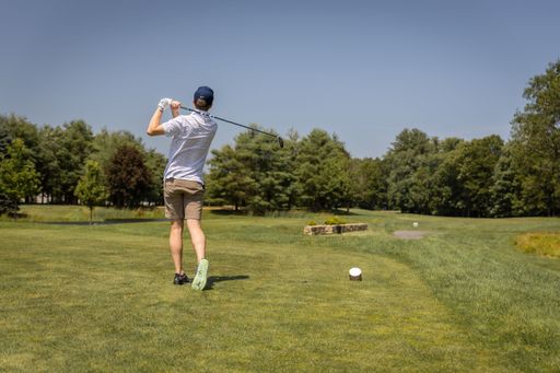 A closeup of a male individual teeing off on a golf course, in front of a lush green landscape