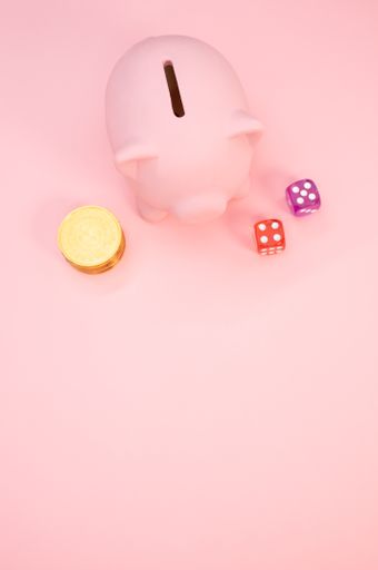 A vertical shot of a piggy bank, dice and a stack of coins on a pink background with space for your text - gambling concept