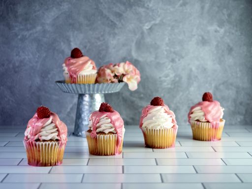 A closeup of raspberry cream flavored cupcakes with fresh flower on the table