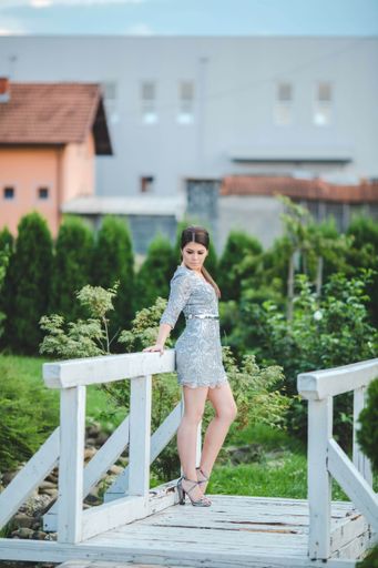 A vertical shot of a beautiful Caucasian woman wearing a silver dress, posing outdoors on a wooden bridge