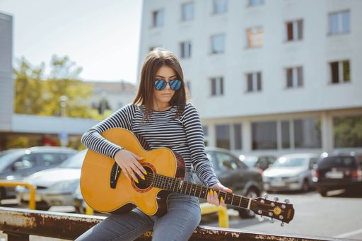 A shallow focus shot of a beautiful Caucasian woman wearing a striped shirt, playing guitar while leaning on a railing