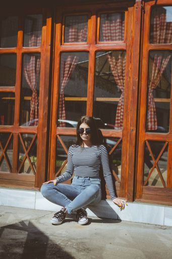 A vertical shot of a cool, fashionable teenager sitting cross legged in front of a rustic door