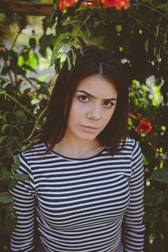 A vertical shot of a beautiful Caucasian woman wearing a striped shirt, posing outdoors against flowers