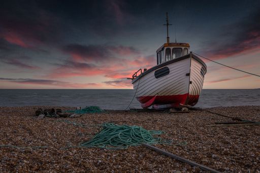 A sailing vessel is beached on a shoreline in a serene coastal setting, with mooring ropes draped across the sand