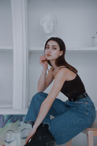 Young and cute girl sitting in a chair in the gallery.
White wall, gypsum head, picture on the floor.