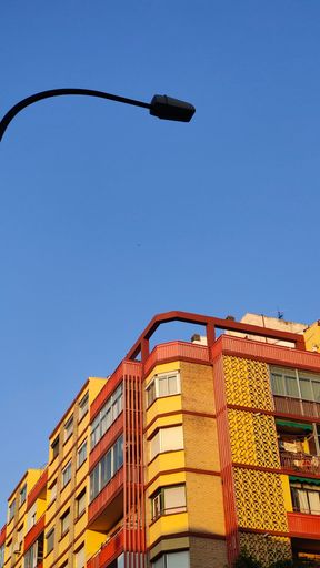 A vibrant blue sky is visible above a residential apartment complex, with a street lamp nearby