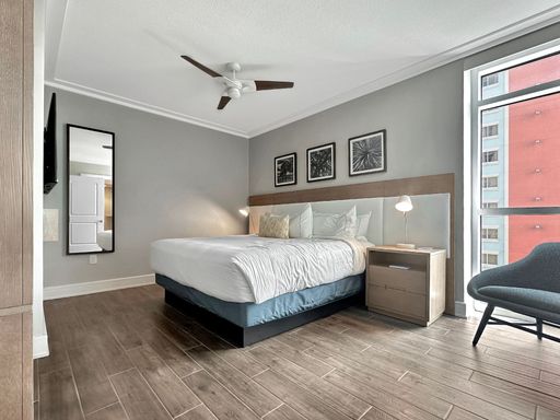 A contemporary bedroom featuring light-wooden flooring and a modern, white bed with a blue comforter