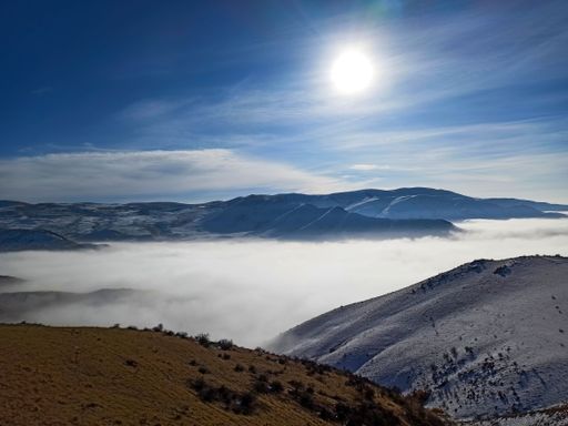 A breathtaking view of snow-covered mountains above the clouds, illuminated by rays of sunlight.