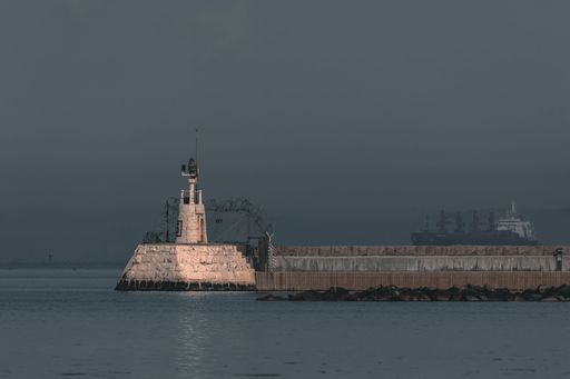 In the distance, a large boat is sailing past, illuminated by both the light of the sea and the lights from the shore