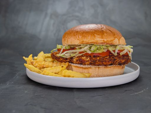 A closeup of a Crispy chicken fillet burger served with French fries on a gray background