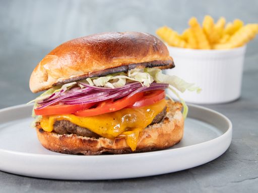 A closeup of a beef burger served with French fries on a gray background