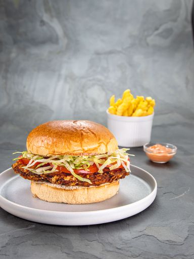 A closeup of a Crispy chicken fillet burger served with French fries on a gray background