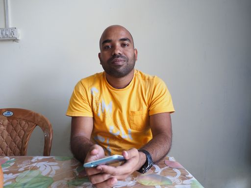 An Indian man sitting in the kitchen with a phone on his hands