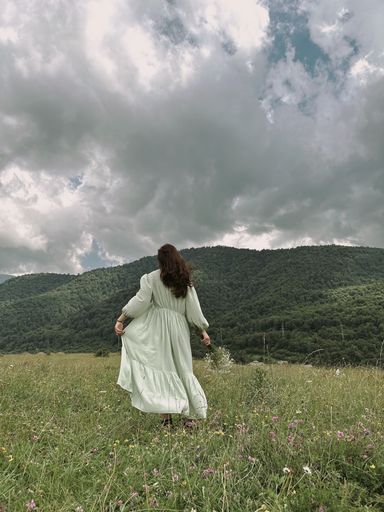 A young woman in a white dress walks in a green field with wildflowers.