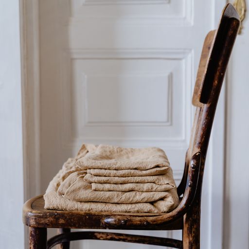 A vertical shot of folded beige bedding on the old wooden chair with a white door in the background