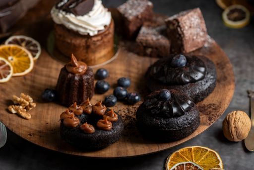 A cakes puddings, chocolate muffins with blueberries, cream cherries, and dried citrus on a wooden plate.