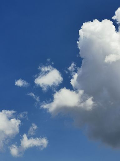A Vertical shot of a vibrant blue sky with fluffy white clouds scattered throughout