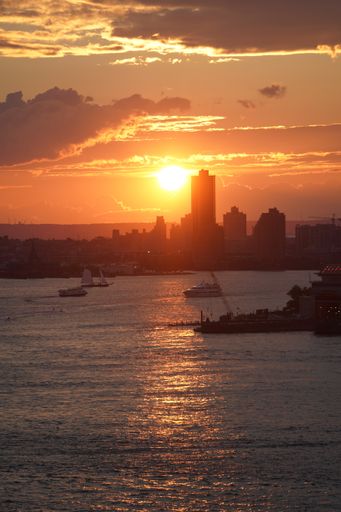 A vertical shot of boats sailing on a sea at sunset near Manhattan, New York skyline