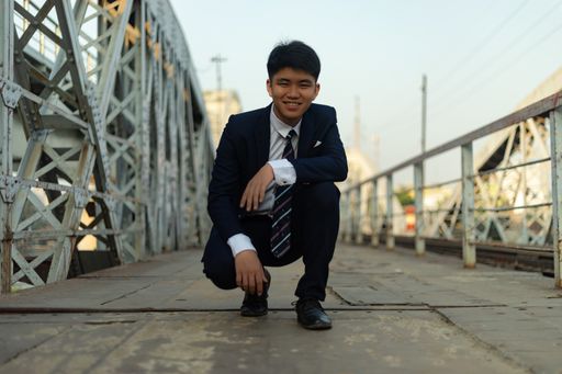 A young Asian man crouched on a bridge with one hand on knee