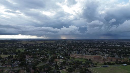 A dramatic sky hangs over a sprawling city and adjacent forest, filled with grey clouds