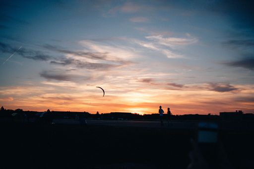 Joggers run across Tempelhofer Feld in Berlin at sunset. Next to the runners Silhoutten lets a man fly a kite.